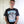 Man wearing a black t-shirt with graphic design and text, standing against a white door.