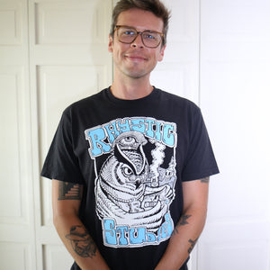 Man wearing a black t-shirt with graphic design and text, standing against a white door.