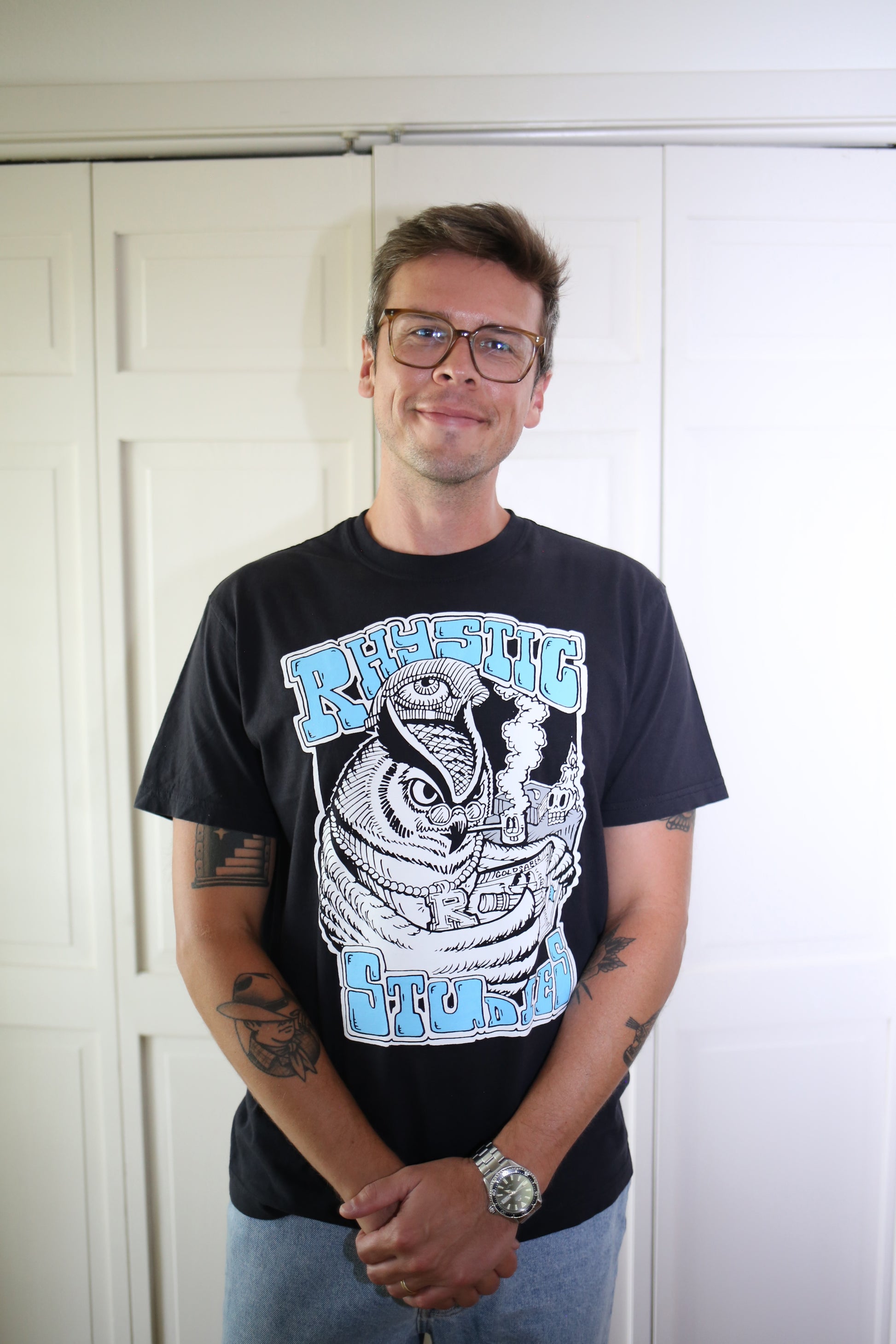 Man wearing a black t-shirt with graphic design and text, standing against a white door.